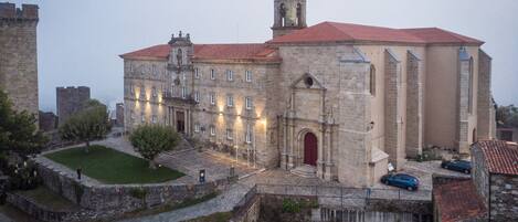 A historic building with a red-tiled roof, a central tower, and a courtyard with a fountain.