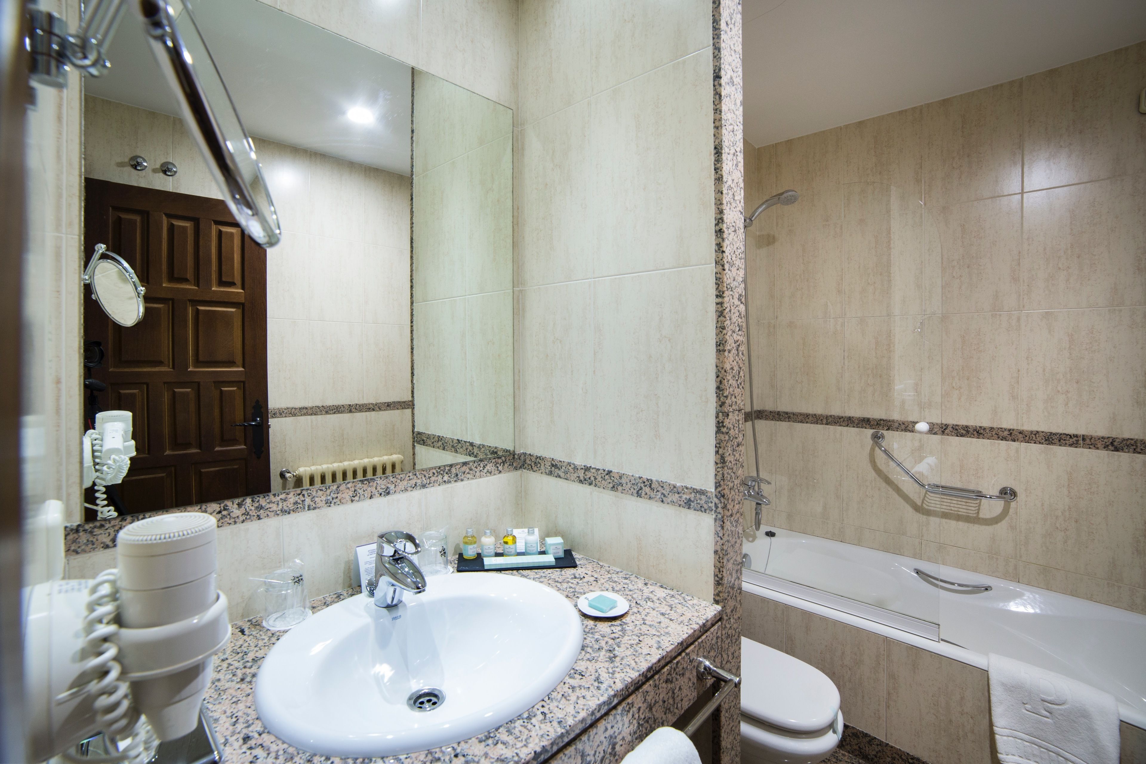 A bathroom with a sink, mirror, toiletries, and a bathtub.