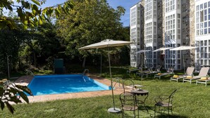 A swimming pool with lounge chairs and umbrellas, surrounded by a grassy area and trees, with a stone building in the background. - Parador De Monforte De Lemos (Monforte de Lemos)