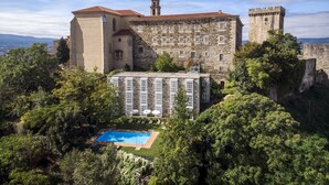 A historic building with a stone facade, a tower, and a swimming pool surrounded by lush greenery. - Parador De Monforte De Lemos (Monforte de Lemos)