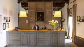 A reception desk with a wooden finish, two pendant lights, a framed portrait above, and a vase with flowers on the counter. - Parador De Monforte De Lemos (Monforte de Lemos)