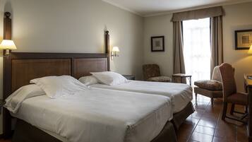 Habitación de hotel con dos camas, una silla, una mesita y una ventana con cortinas.