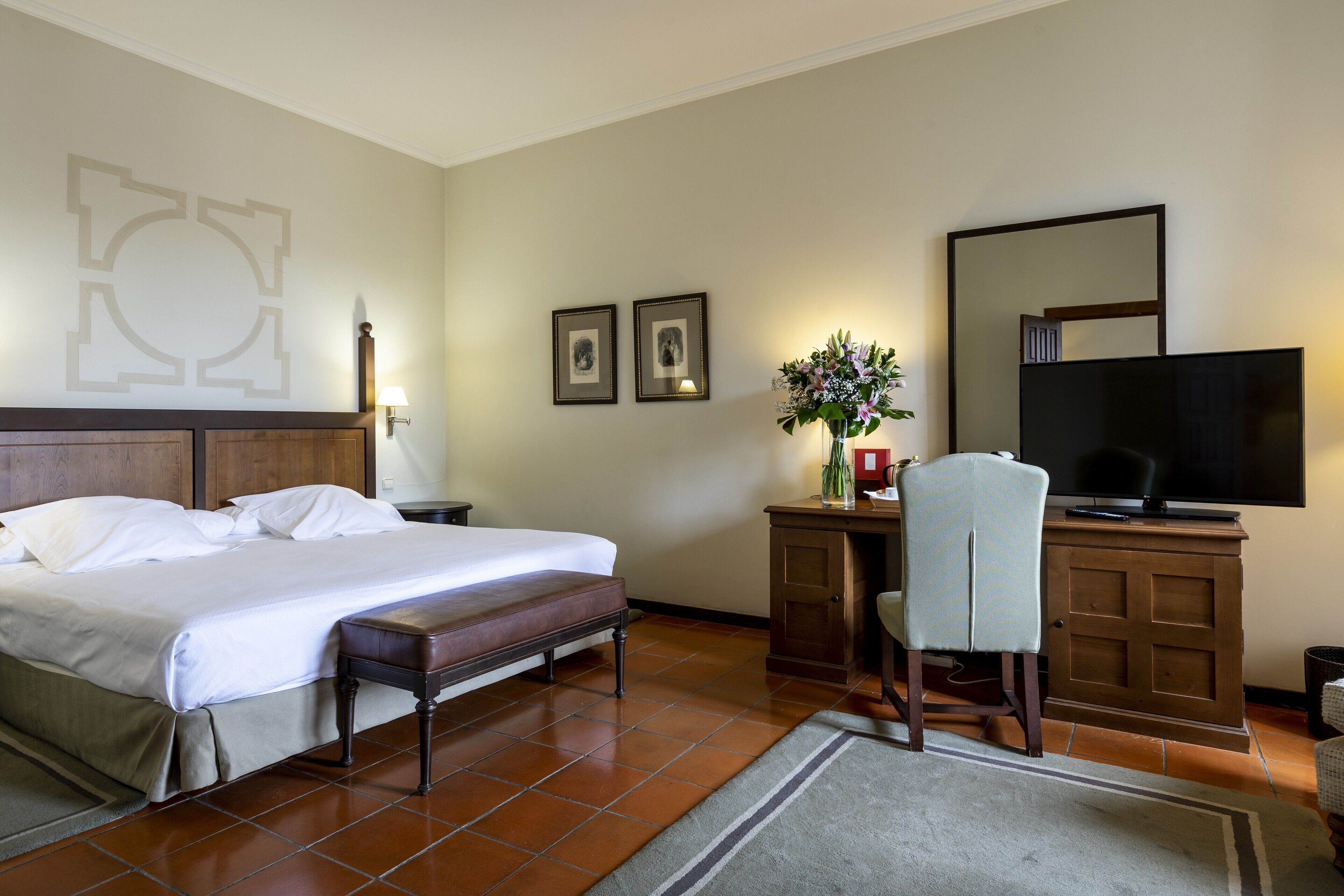 Una habitación de hotel con cama, escritorio, silla, televisor y espejo instalado en la pared.