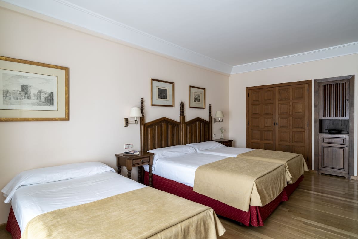 Quarto de hotel com duas camas, cabeceiras de madeira, quadros nas paredes, guarda-roupa de madeira e um pequeno armário.