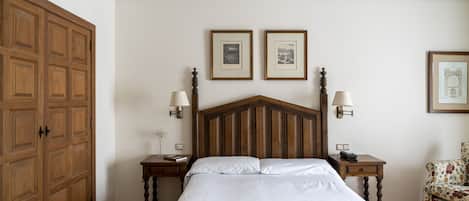 A bedroom with a wooden headboard, two bedside tables with lamps, a bed with white linens, and two framed pictures on the wall.