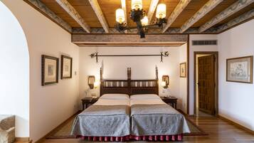 Un dormitorio con dos camas, vigas de madera, una araña, cuadros enmarcados y una alfombra estampada.