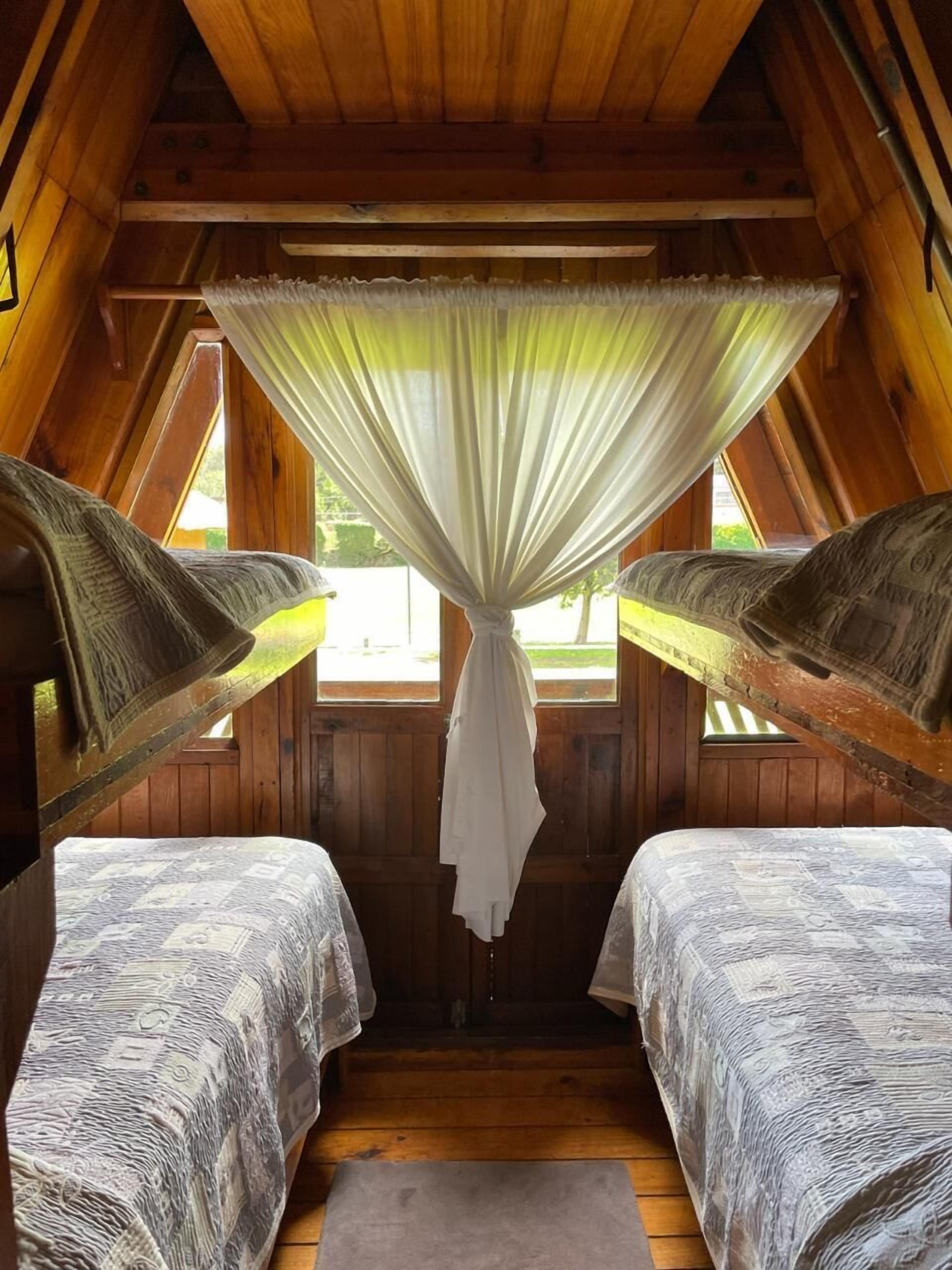 Un dormitorio acogedor en el desván con dos camas, vigas de madera y vistas por una ventana.