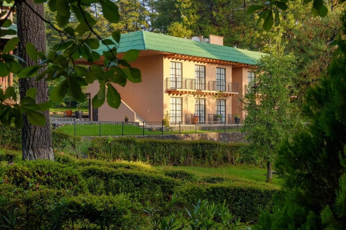 Un edificio de dos pisos con techo verde, rodeado de setos y árboles bien cuidados.