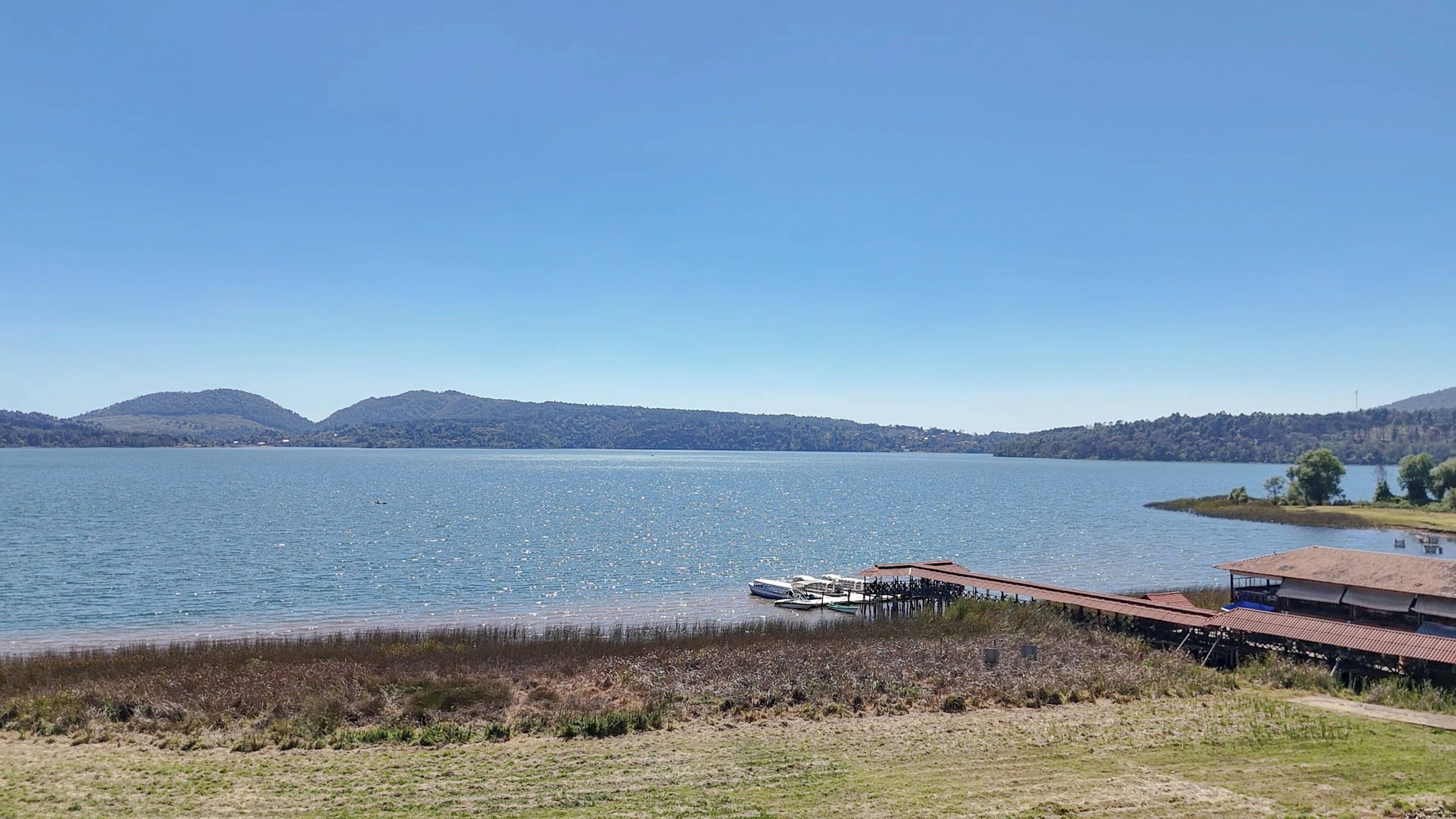 A lakeside view with a dock, boats, and a building with a red roof.