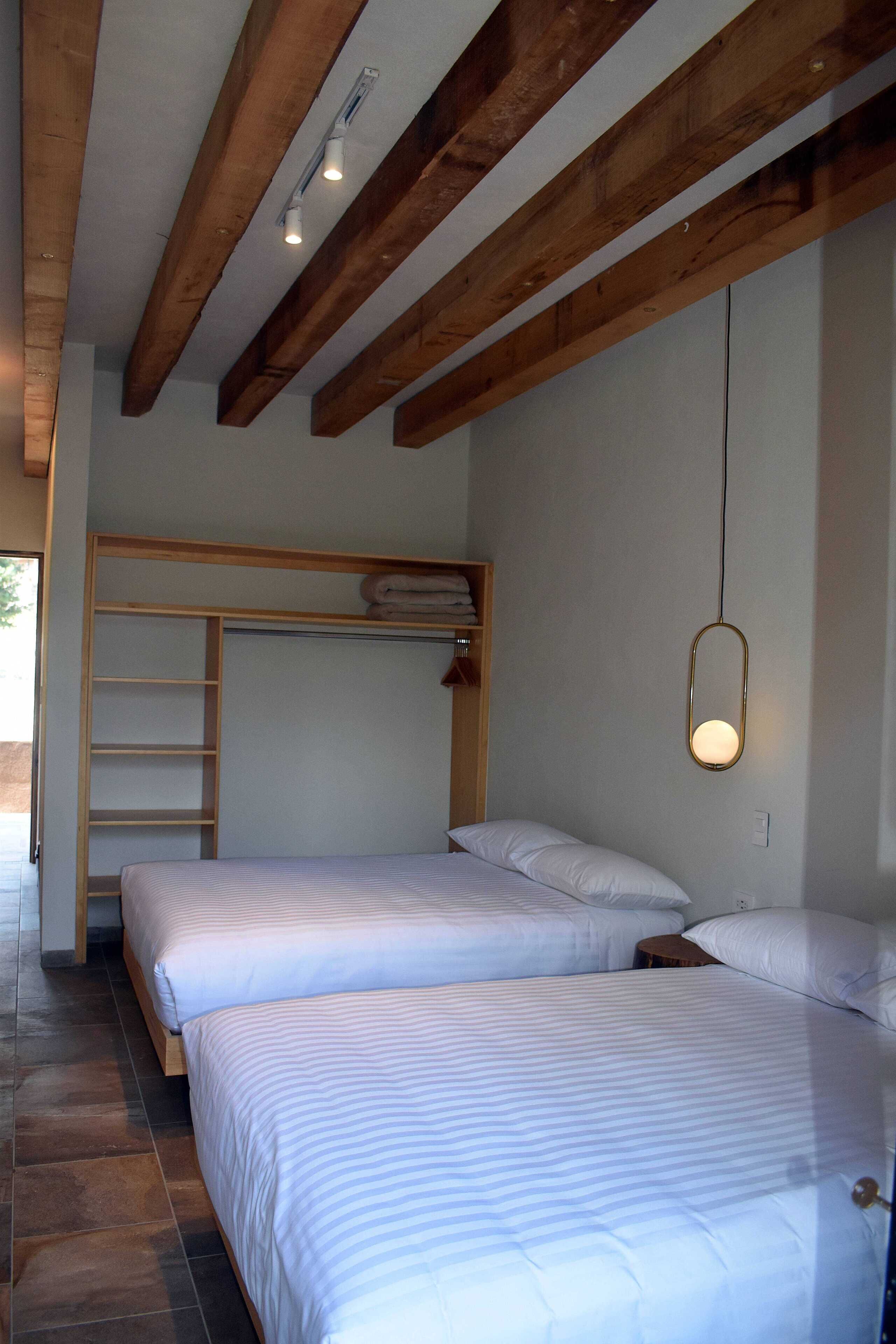 Une chambre avec deux lits, des poutres apparentes, un luminaire suspendu et une étagère intégrée où sont rangées des serviettes.