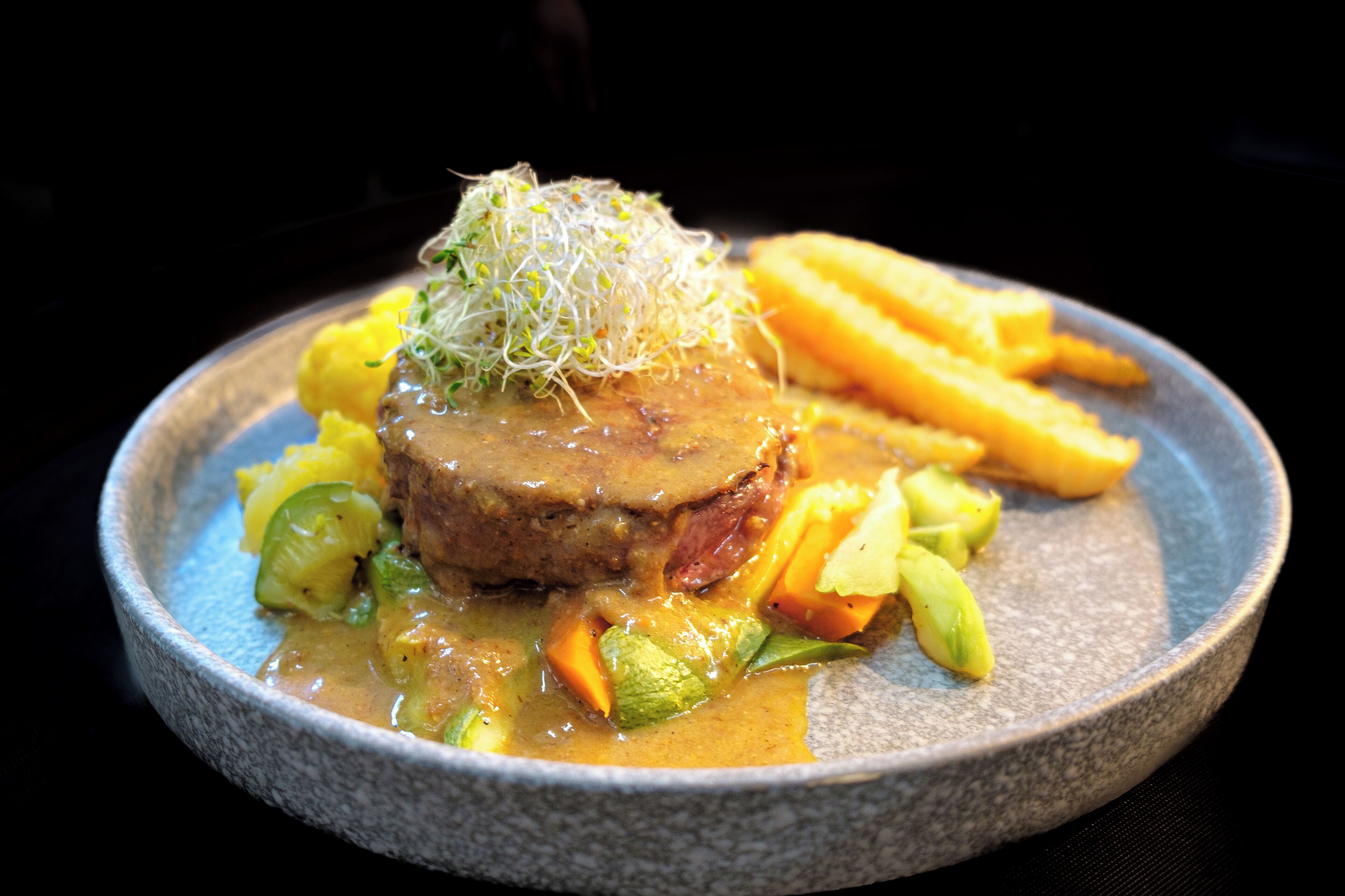 Un plato de comida con un guiso de carne, verduras y papas fritas.