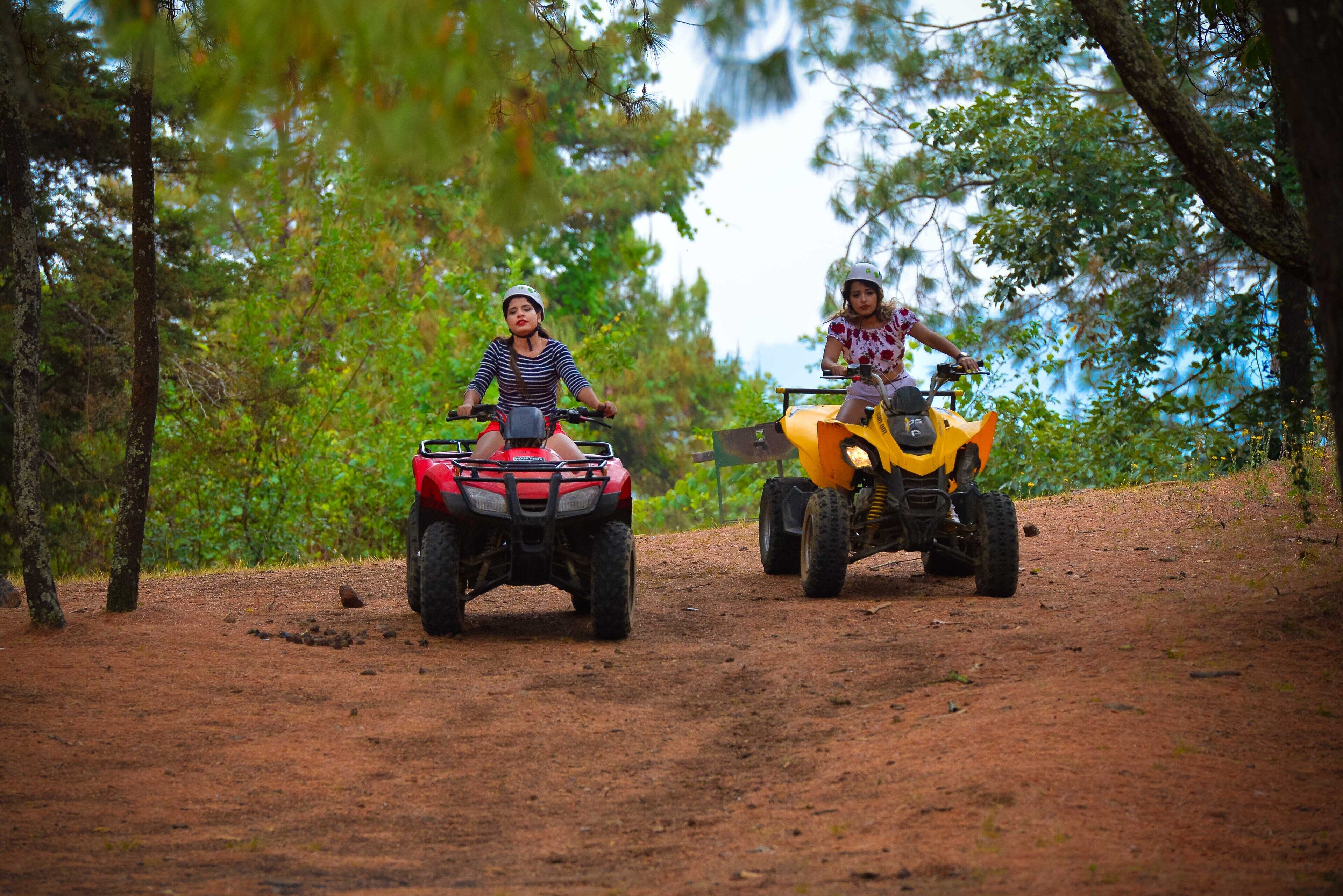 Two people riding ATVs on a dirt path surrounded by trees.