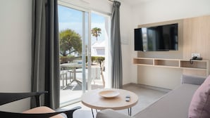 A modern living room with a sofa, a round table, a TV mounted on the wall, and a sliding glass door leading to an outdoor area. - Apartamentos Santa Rosa (Teguise)