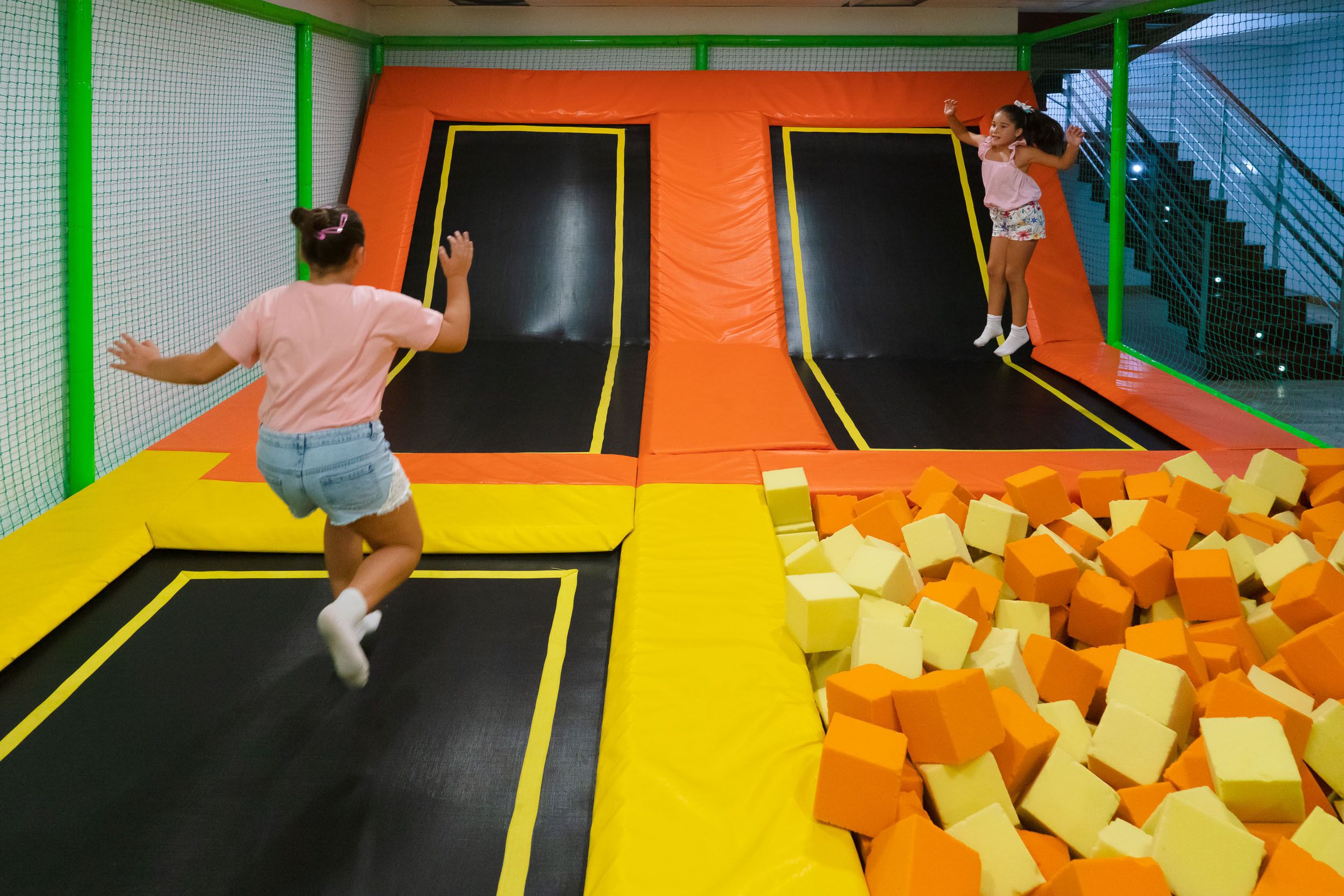 Zona de trampolines con red de seguridad y bloques de espuma.
