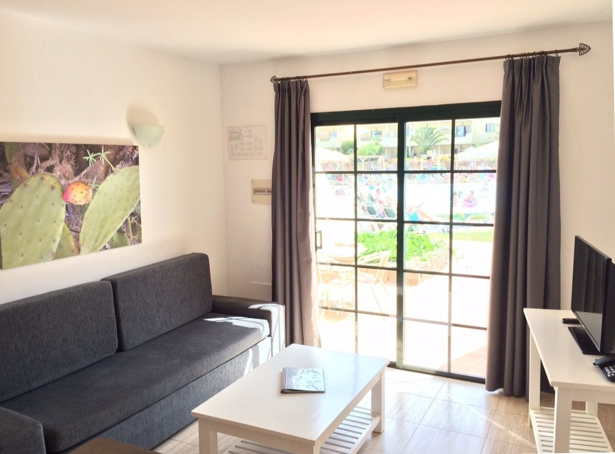 Una sala de estar moderna con un sofá gris, una mesa de centro blanca y un televisor sobre un mueble.