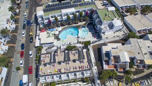 An aerial view of a hotel with a swimming pool, multiple floors, and a parking lot. - Apartamentos La Moraña (Tías)