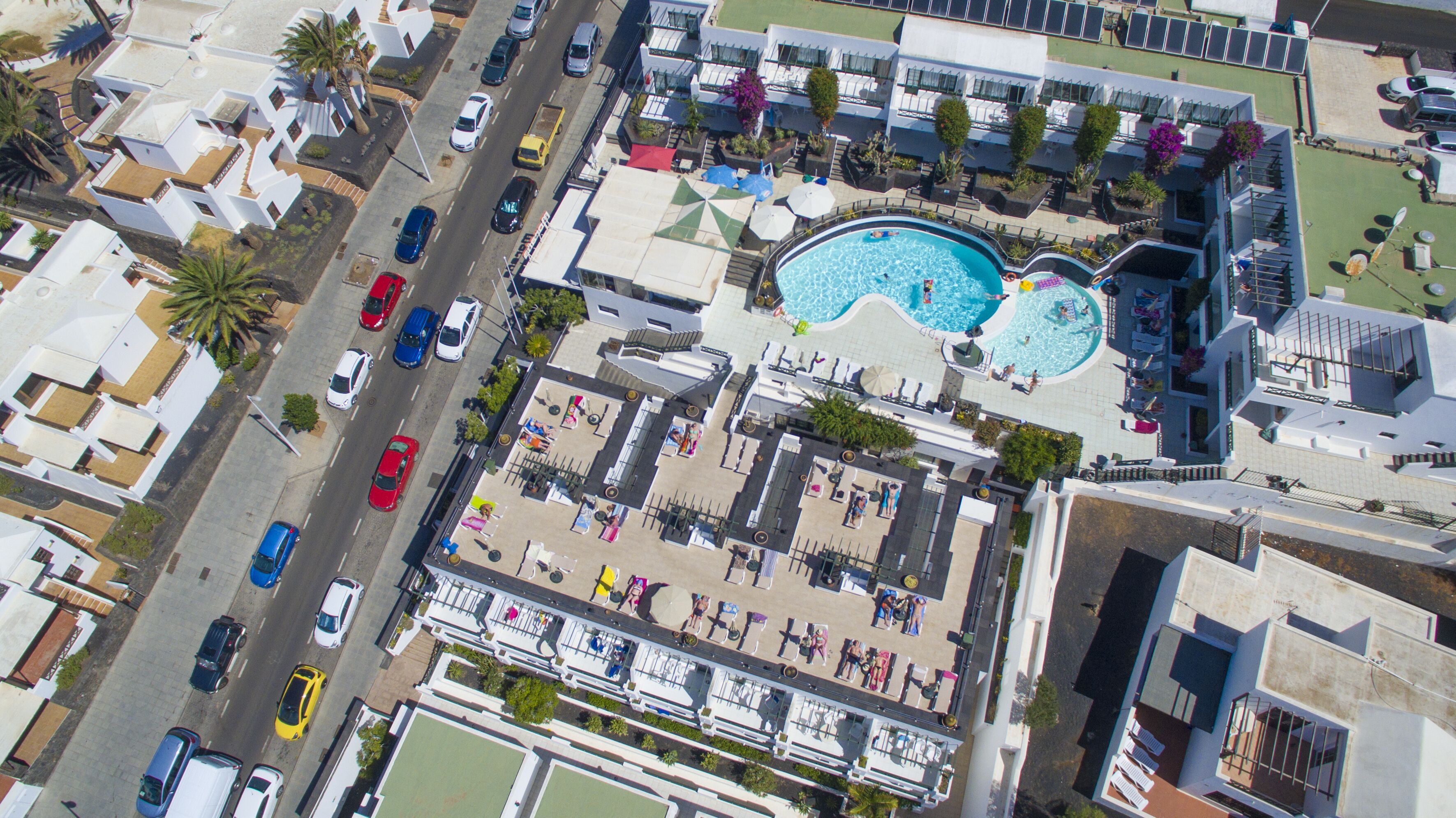 An aerial view of a hotel with a swimming pool, outdoor seating, and a parking area.