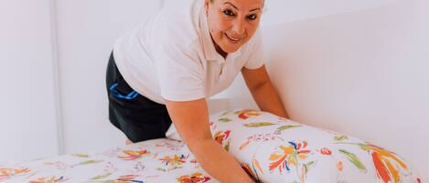 Una persona acomodando una colcha con estampado floral en una habitación de paredes blancas.