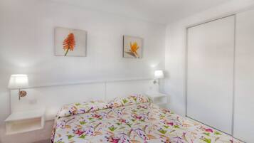 Un dormitorio con colcha estampada, dos cuadros en la pared, una mesita de noche con lámpara y un armario.