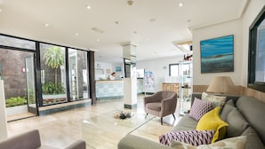 A spacious living area with a sofa, armchairs, and a coffee table. There is a large window with a view of the outdoors. - Apartamentos La Moraña (Tías)