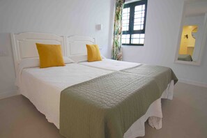 A double bed with white and green bedding, a window with floral curtains, and a mirror on the wall. - Apartamentos La Moraña (Tías)