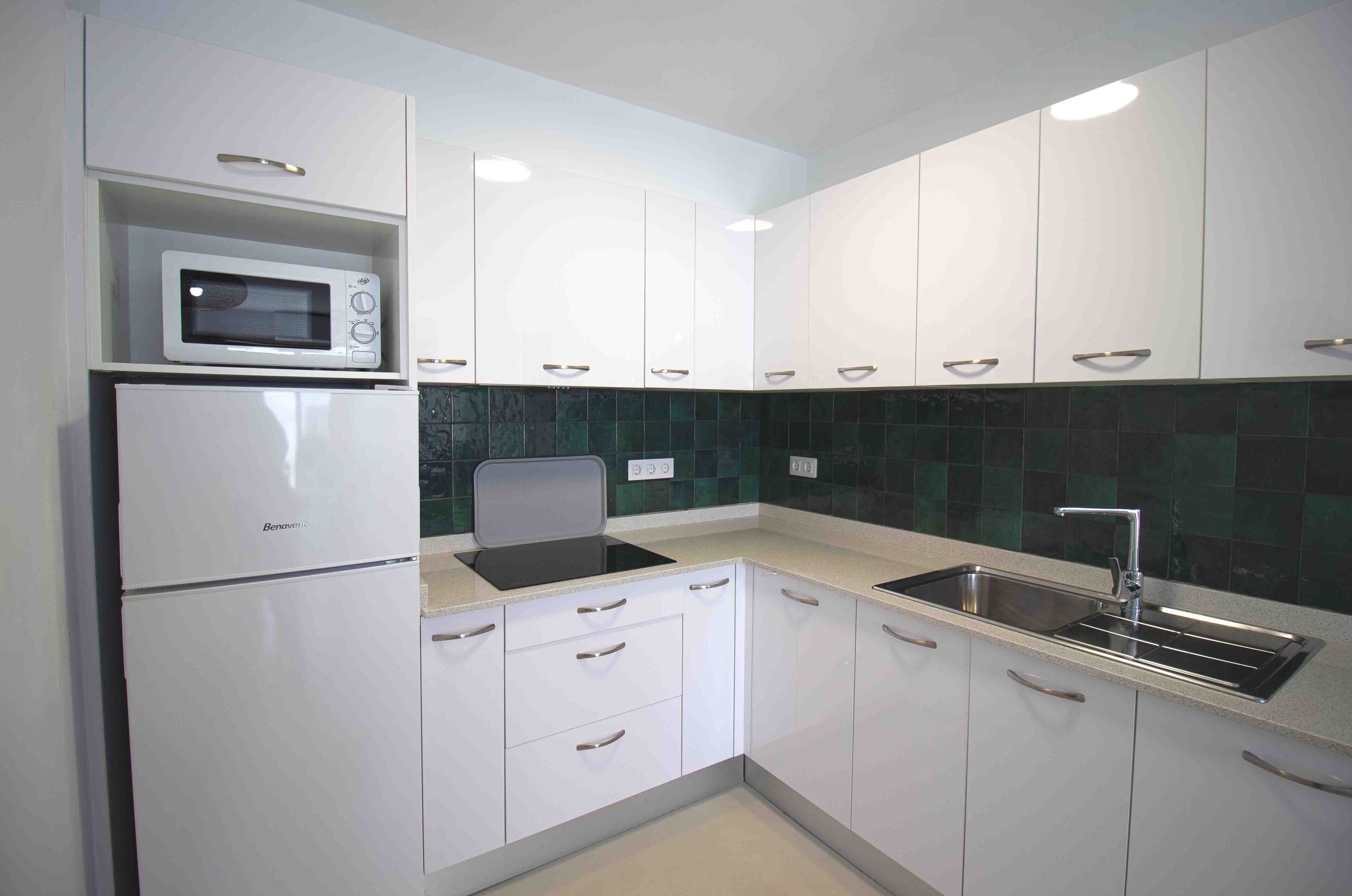 A modern kitchen with white cabinets, a microwave, a sink, and a black countertop.