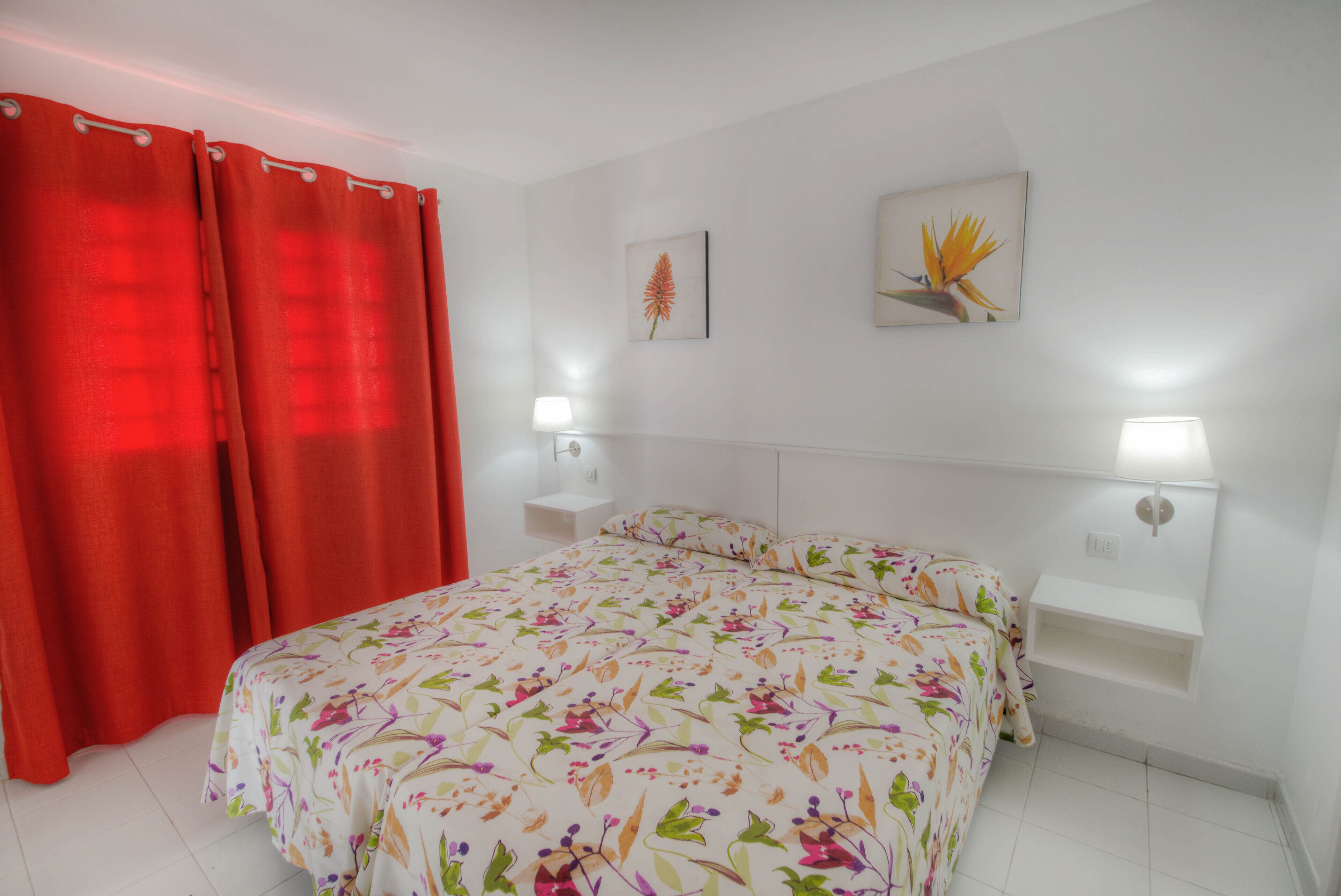 Un dormitorio con colcha estampada, dos lámparas de noche, una mesita de noche y una cortina roja.
