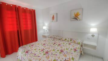 Un dormitorio con colcha estampada, dos lámparas de noche, una mesita de noche y una cortina roja.