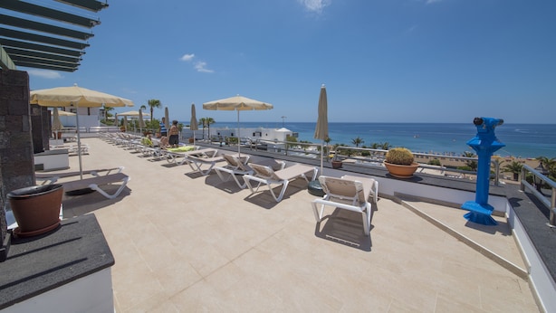 A rooftop terrace with lounge chairs, umbrellas, and a view of the ocean. - Apartamentos La Moraña (Tías)