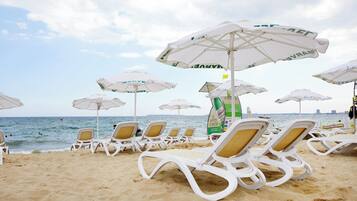 Beach chairs and umbrellas arranged on a sandy beach with the sea in the background.