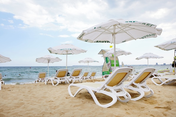 Beach chairs and umbrellas arranged on a sandy beach with the sea in the background. - Marvel (Nessebar)