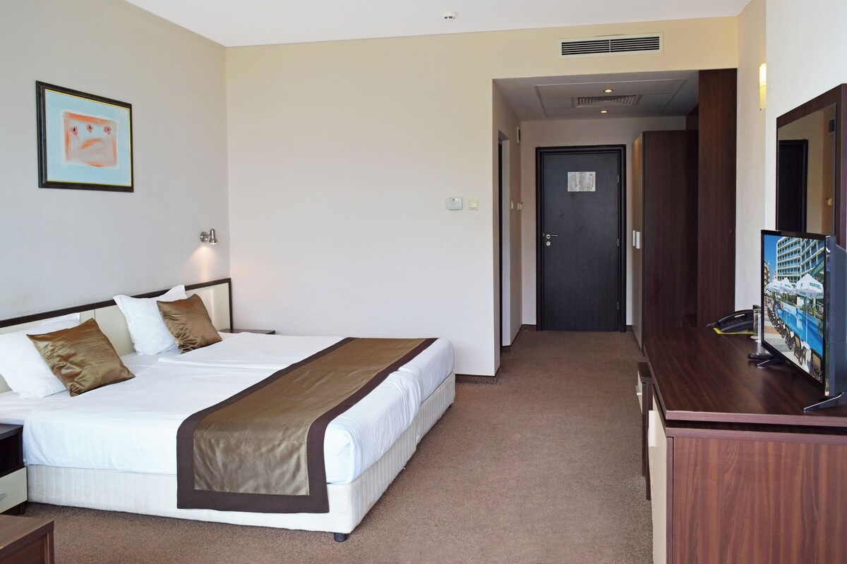 A hotel room with a bed, a TV, a desk, and a door leading to another room.