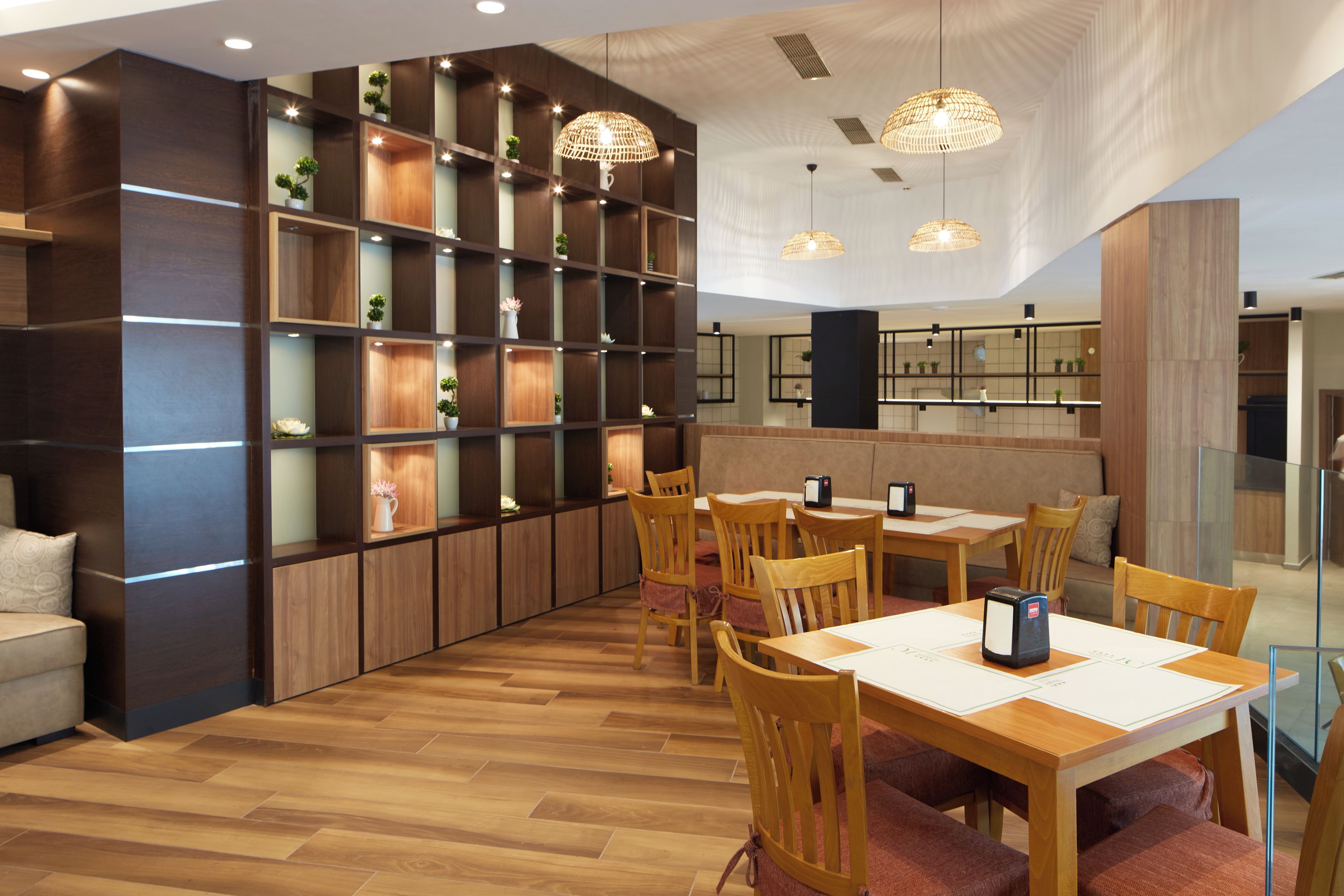 Un moderno vestíbulo de hotel con suelo de madera, un área de estar con mesas y sillas, y una amplia estantería llena de objetos decorativos.