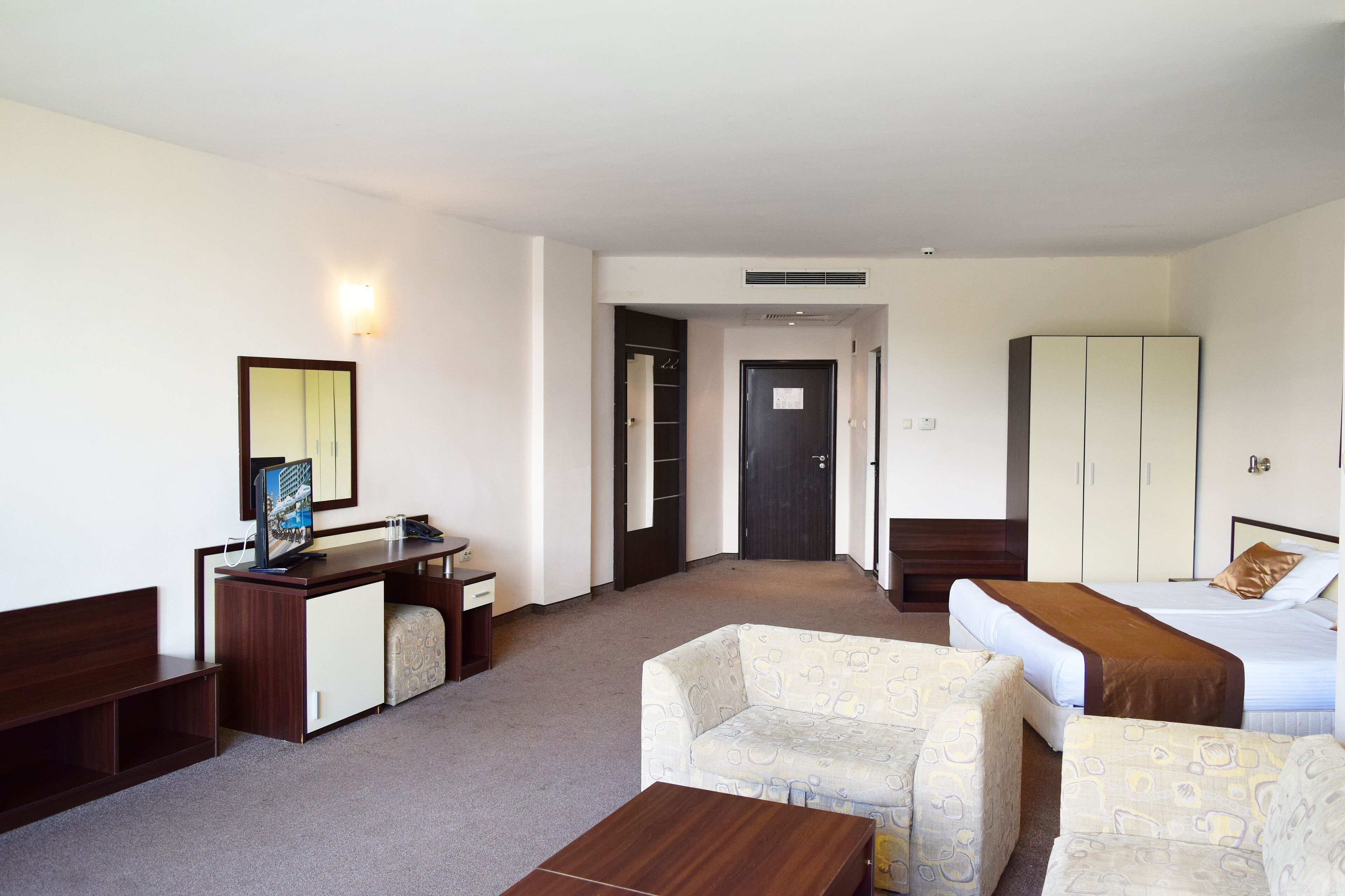 A hotel room with a bed, a desk, a chair, a sofa, and a wardrobe.