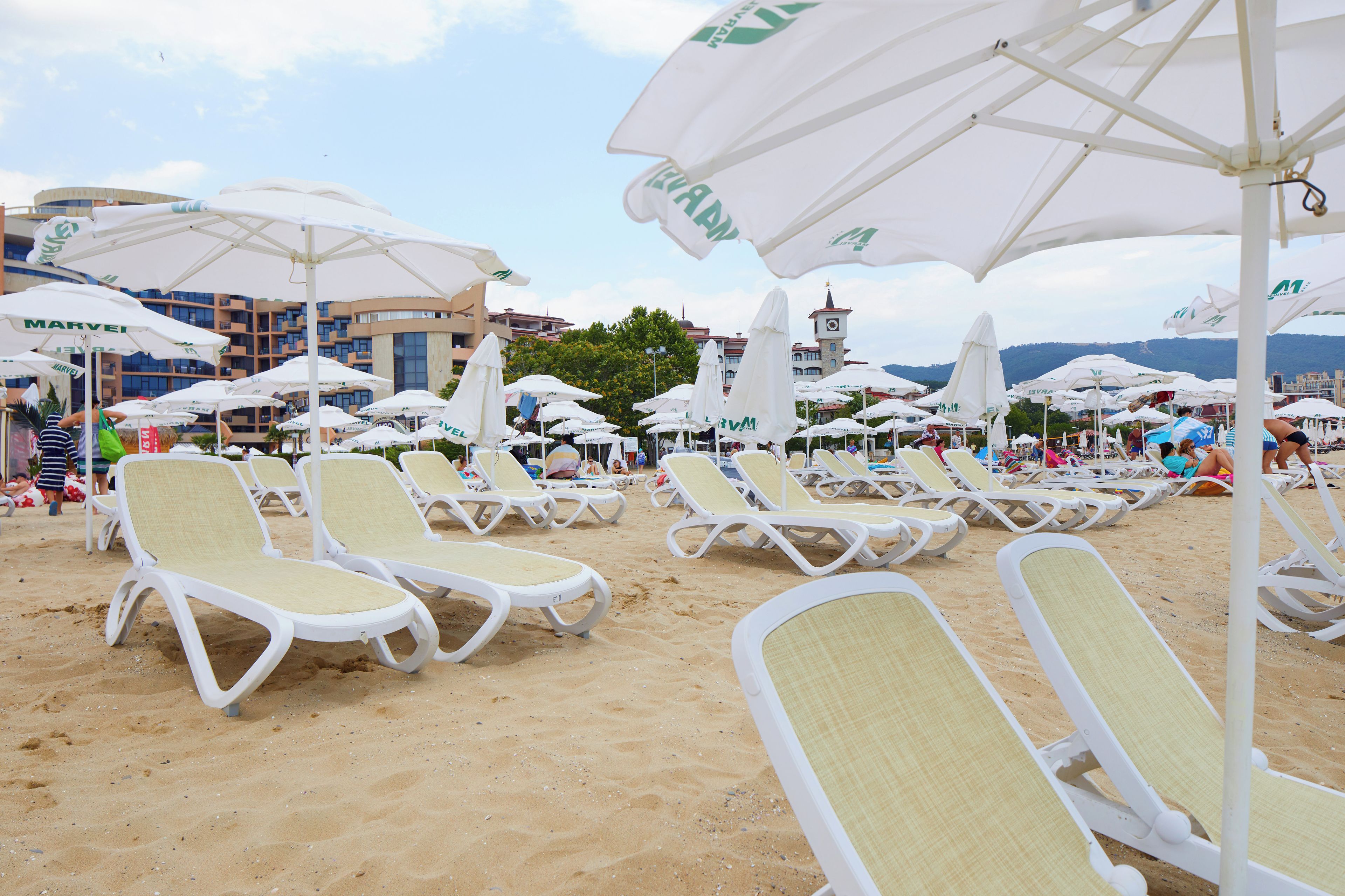 A beach with rows of sun loungers and umbrellas, some with visible branding.