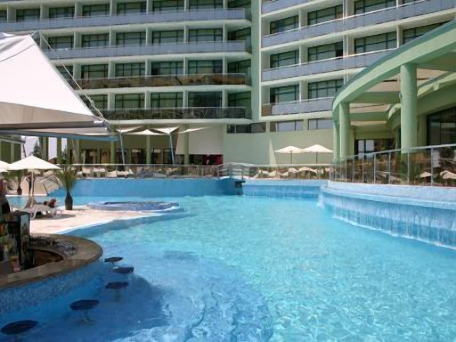 Un hotel con una amplia piscina cubierta, varios balcones y sombrillas.