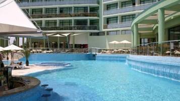Un hotel con una amplia piscina cubierta, varios balcones y sombrillas.
