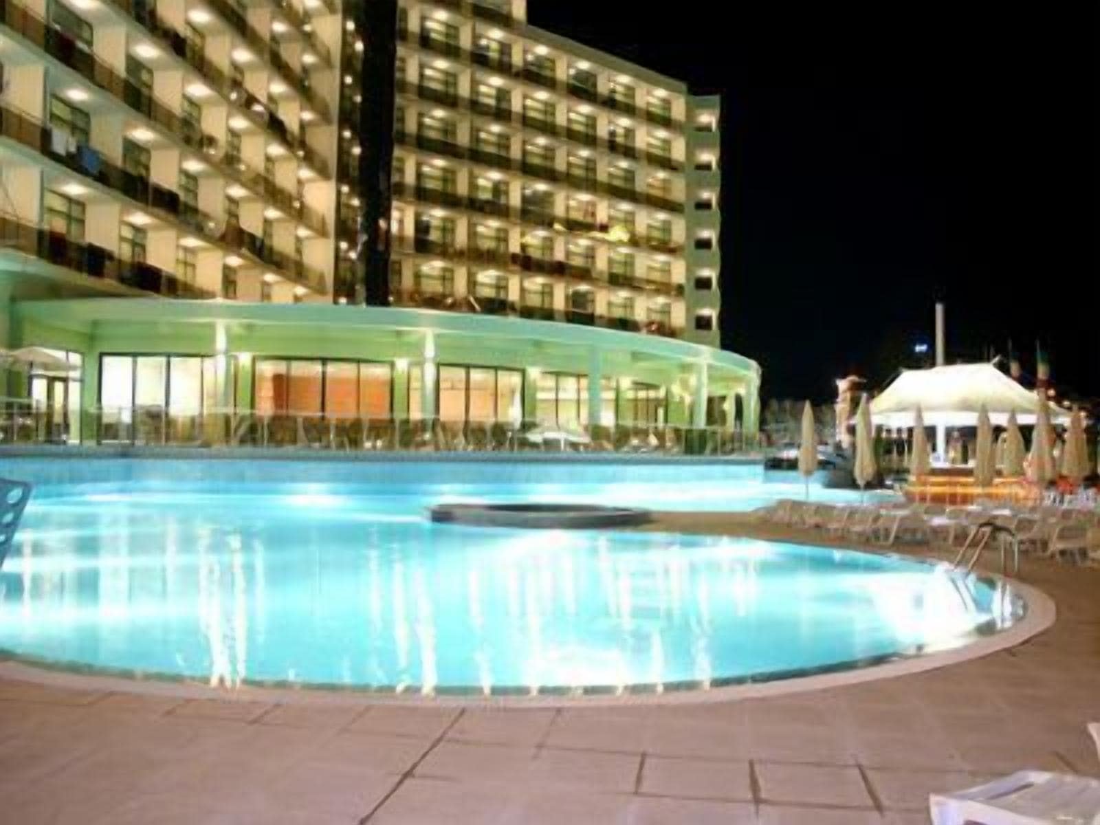 A swimming pool with lounge chairs and umbrellas, surrounded by a building with multiple floors and balconies.