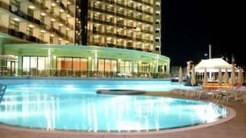 A swimming pool with lounge chairs and umbrellas, surrounded by a building with multiple floors and balconies.
