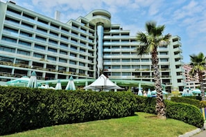 A multi-story hotel with a central atrium, outdoor seating area, and palm trees. - Marvel (Nessebar)