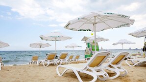 A beach with rows of white lounge chairs and white umbrellas with green text. - Marvel (Nessebar)