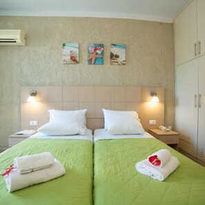 A hotel room with two beds, green bedding, white pillows, a wooden headboard, wall-mounted artwork, bedside lamps, a nightstand, and a wardrobe.