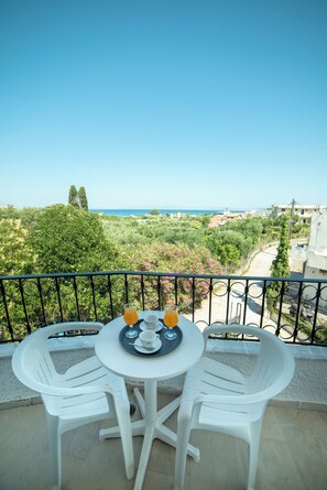 A balcony with a table and two chairs, overlooking a scenic view of greenery and buildings. - Alkionis (Corfu)