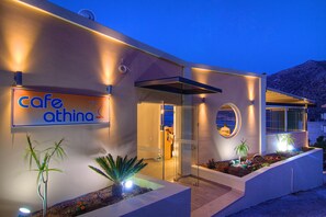 A modern building with a cafe named 'cafe athina' sign, a glass entrance, and a landscaped area with plants. - Aparthotel Athina (Mylopotamos)