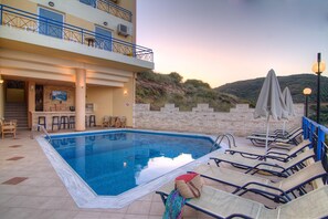 A swimming pool with lounge chairs and umbrellas, a bar area, and a view of a hillside. - Aparthotel Athina (Mylopotamos)
