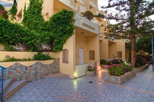 Un edificio con un muro de piedra, un patio con baldosas y un balcón con plantas.