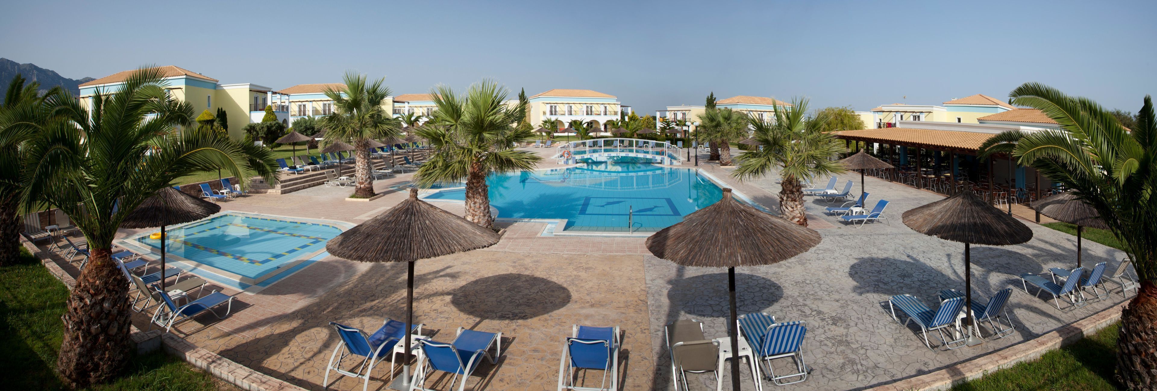 A resort with a central swimming pool surrounded by lounge chairs and palm trees.