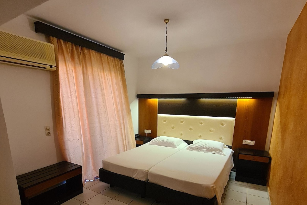 Une chambre d’hôtel avec un grand lit, une table de chevet, un banc et un luminaire au plafond.