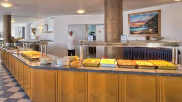 Una mesa de buffet con diversos alimentos y un cocinero cerca.