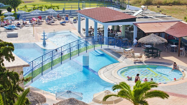 A resort pool area with multiple swimming pools, lounge chairs, umbrellas, and dining tables. - Corali Hotel (Kos)